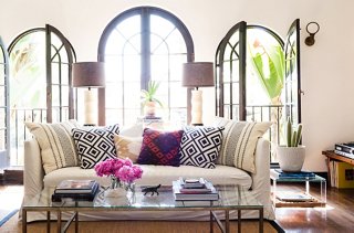 A glass coffee table and Lucite side tables make for an airy feel, while graphic pillows mirror the architectural details of the windows.
