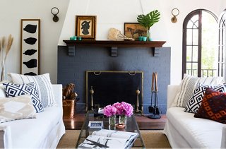 The painted brick fireplace is the focal point of the living room. Flanking it are Circa Lighting sconces Lizzie chose for their nautical form and vintage look.
