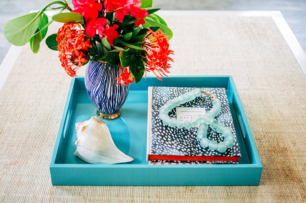 A string of beads in sea-glass blue and a vase of tropical flowers create a focal point atop the living room coffee table. The raffia surface adds relaxed, earthy texture to the space.
