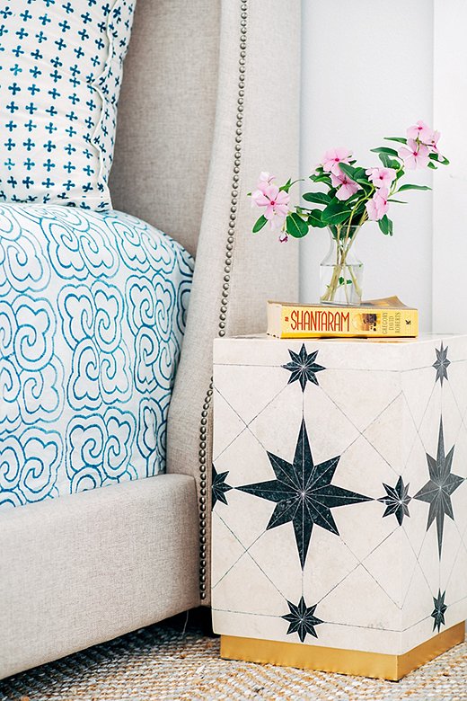 A side table with a black-and-white geometric pattern is an unexpected—yet decidedly chic—choice for a nightstand. The bed’s neutral upholstery lets the blue-and-white linens take center stage.
