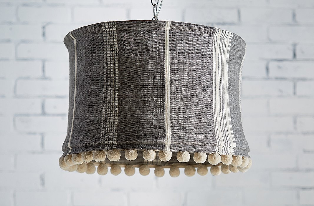 The Sutton Slipcover Pendant features a striped organic-cotton shade trimmed in cheerful pompoms. The fabric is hand-dyed and handwoven by skilled artisans in Ethiopia.
