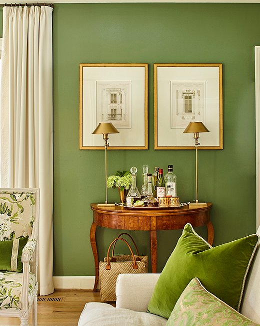 Minnette craved a color that was “rich but not overwhelming,” and landed on this particular hue (Farrow & Ball’s Calke Green) after seeing images of the green velvet-lined living room of designer Veere Grenney. Slim brass lamps (the Hayes table lamp by Chelsea House is similar) provide a cool counterpoint to an antique French demilune and a pair of French architectural engravings.
