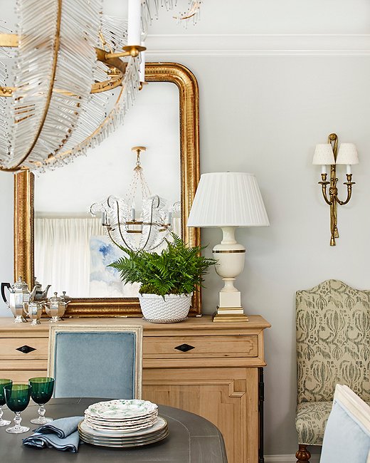 A large gold Louis Philippe mirror, a lucky French flea market find, leans casually atop the sideboard. Vintage sconces help create an inviting glow for evening gatherings.
