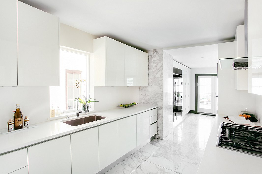 Sleek white surfaces and lots of closed storage keep this narrow kitchen from feeling cluttered. Post-renovation, the space opens onto a sunlit breakfast room, with French doors that lead to the patio.
 
