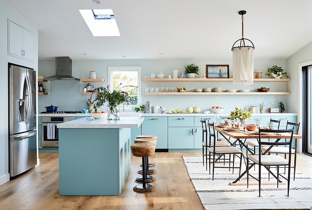 With plenty of space for friends and family to hang out while Minnie cooks, the revamped kitchen is entertaining-central: “It’s so convivial,” Minnie says. Cheery blue lower cabinets combined with light-toned open shelving help the small space feel airy and open, while accents of dark metal in the chairs and the pendant light lend an edge to the seaside scheme. Sleek sink fittings and hardware by Waterworks help complete Minnie’s ideal “cook’s kitchen.”
&nbsp;
&nbsp;
