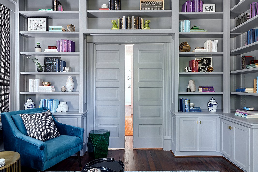 “My clients loved the charm in here,” says Elizabeth of the library, which is right off the home’s foyer. “It is the first thing you see when you walk in, so we wanted this room to pop.” She painted both the entry and the library a lush gray, carrying the color onto the bookshelves, doors, and moldings to create an enveloping feel. Blue and purple accents complement the paint’s cool undertones.
