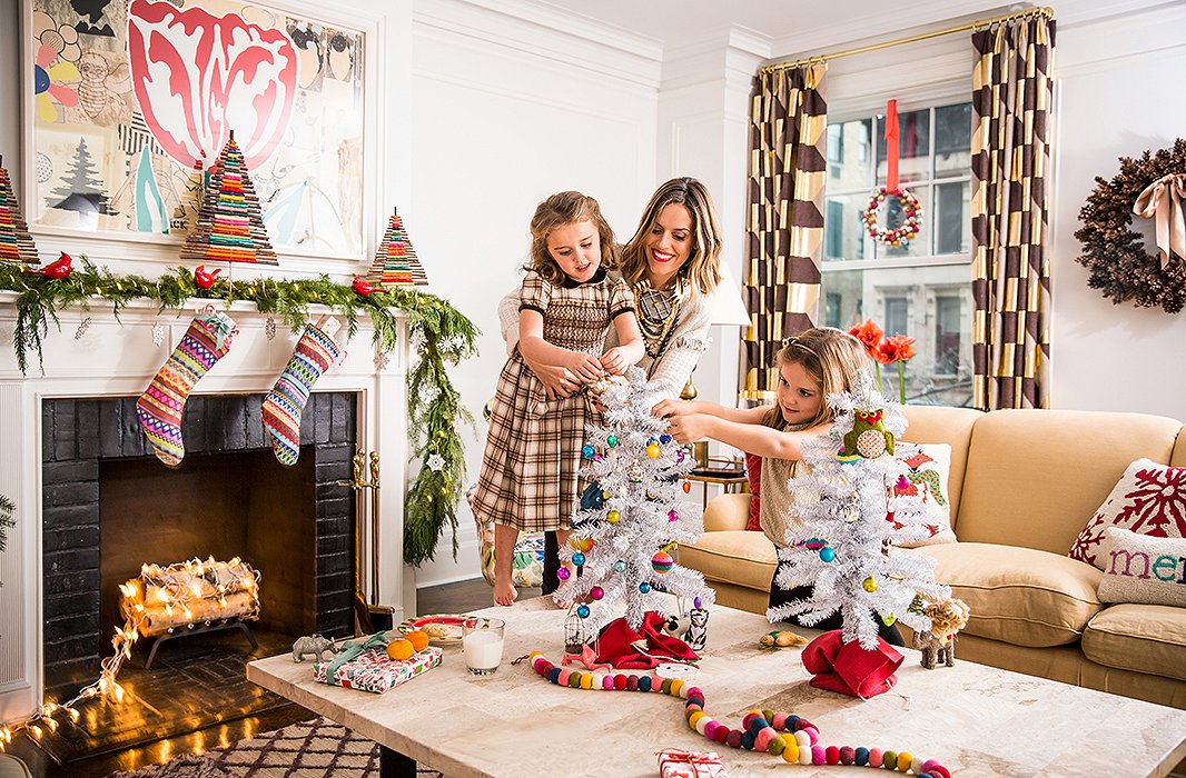 “Holiday decorating with the girls is so much fun,” says Lilly, here seen helping Daisy and Grace with the top of a tree. (And note the surprising and fun use of electric lights in the fireplace.)
