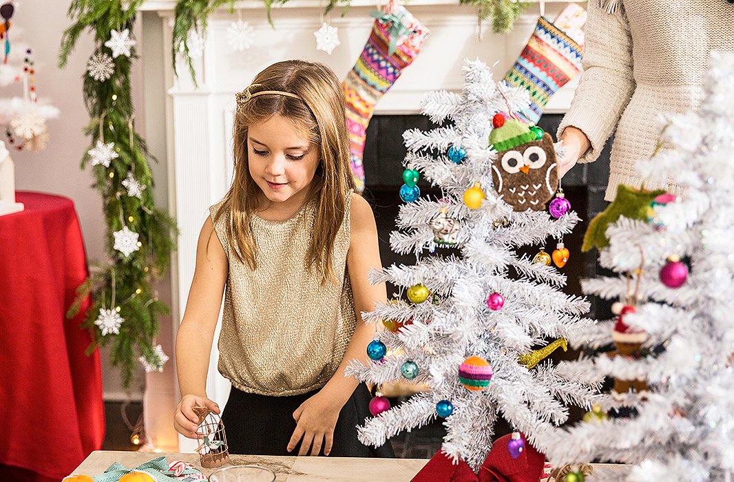 In front of the fireplace, which is dressed up with garland and glitzed up with silver ornaments, Grace prepares to place a birdcage ornament.
