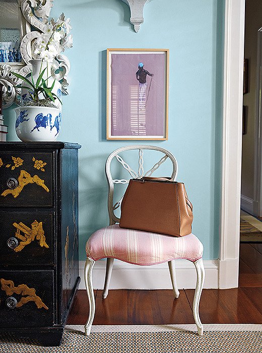 A vanity chair in a guest bedroom functions as both a beautiful perch and a holding spot for bags and coats. Its chipped white-painted frame recalls a gesture favored by famed decorator Dorothy Draper.
