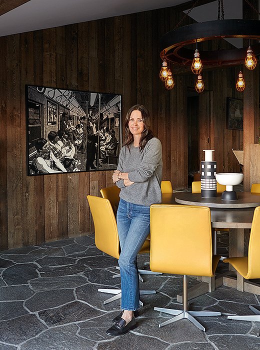 Yellow chairs on sleek chrome bases enliven the dining room’s wood-paneled walls and stone floors.
