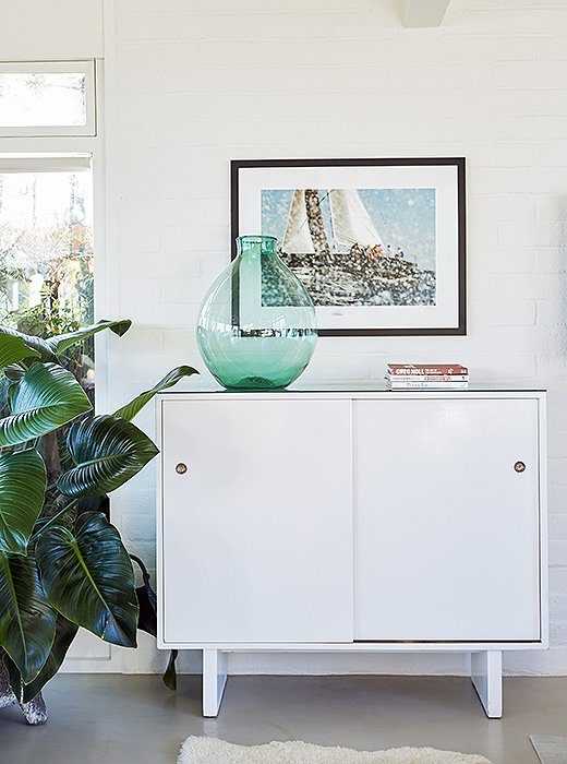 Nautical artwork and a green glass jug play up the beach-house vibe atop a white Widdicomb cabinet.
