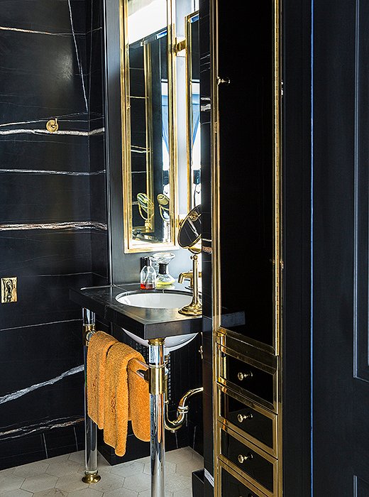 A black marble powder room with brass accents offers a stylish spot to freshen up. A hint of orange, similar in hue to what’s seen in the dining room library, appears in a set of hand towels. 
