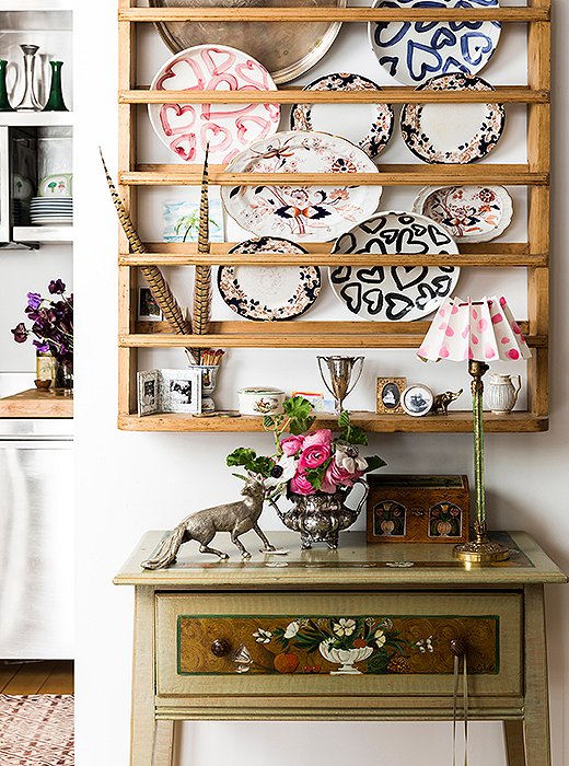 A Scandinavian pine plate rack from Design Works in Cape Cod hangs on a wall adjacent to the dining area—a perfect piece for someone with a penchant for painted plates (the ones with hearts are her own design). Below, a table painted by a family friend hosts a silver fox and an antique vase. The lamp? Vintage, crowned with a shade Kate made with folded paper, velvet ribbon, and Scotch tape. 
