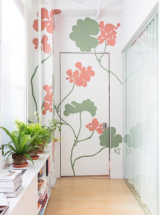 In a hallway connecting the master bedroom to the living room, Kate transformed a seldom-used door with a mural of geraniums painted in her signature larger-than-life scale, creating “a nice focal point.” She adds, “I never sketch my murals. They’re always improvised in the moment… I’ll climb up a ladder with a bunch of plants or flowers nearby and paint how I see them up on the wall.” 
