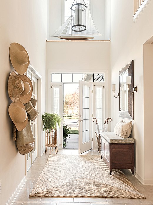 The light-suffused entry at Matthew Caughy’s beach house sets off the home’s welcoming, at-ease vibe with soaring ceilings, a natural-fiber rug, and an antique bench, found at a local shop, that holds board games often brought out for little ones in the family. The sconces are by Visual Comfort.
