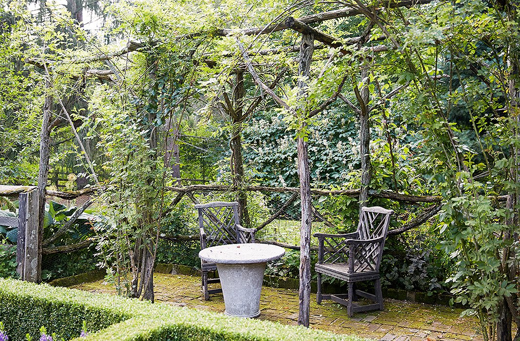 Antique chairs and a stone table beneath a rustic pergola, made from locust saplings that had been cut down, provide a quiet resting spot in the formal garden.

