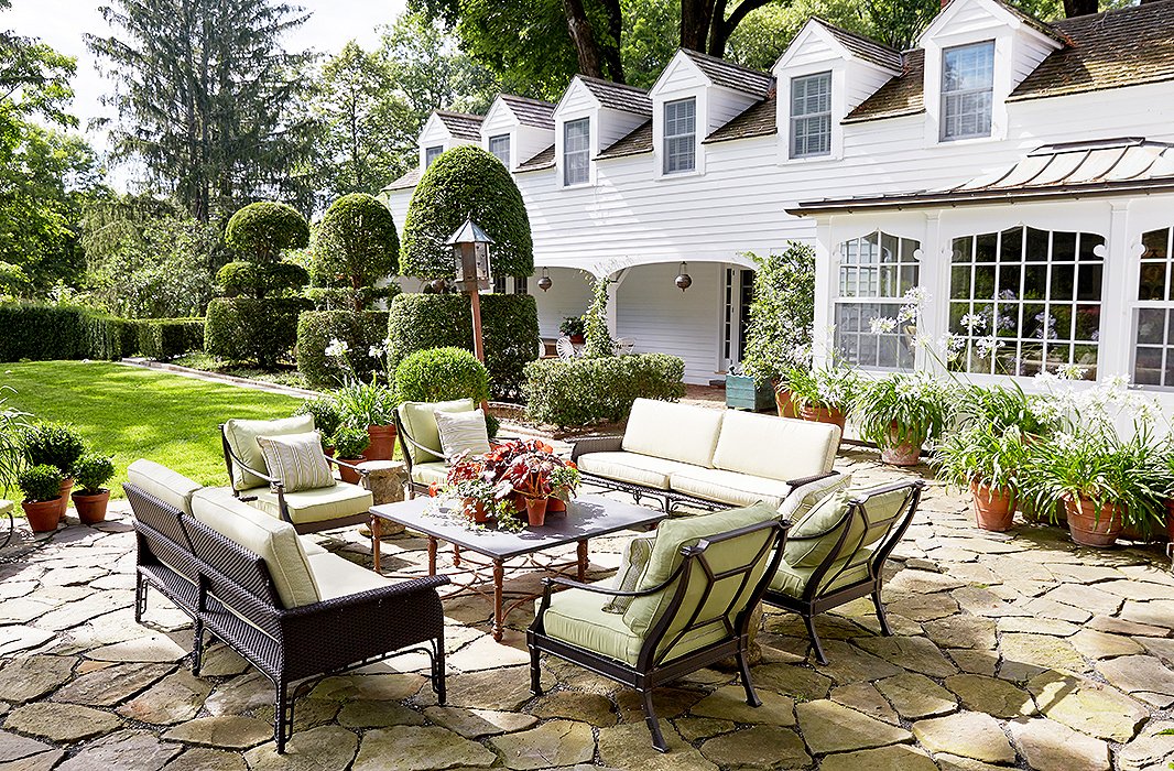 A stone terrace just off the main house was transformed into an outdoor room with comfy sofas designed by Bunny along with chairs in matching cushions. Groupings of terracotta planters help round out a lush, lived-in ambience. The tall topiary yews date to 1910.
