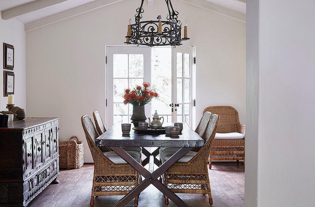 “This is the family table,” says Kendall. “We have dinner, the girls do their homework.” It was reimagined from an antique Spanish door. The rattan chairs add airy space. A vase by potter Miri Mara sits near striped cups by a local artisan.
