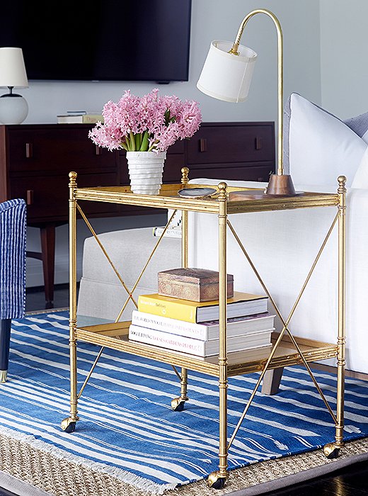 A gold bar cart adds traditional lines as well as surface area for a lamp and drinks.
