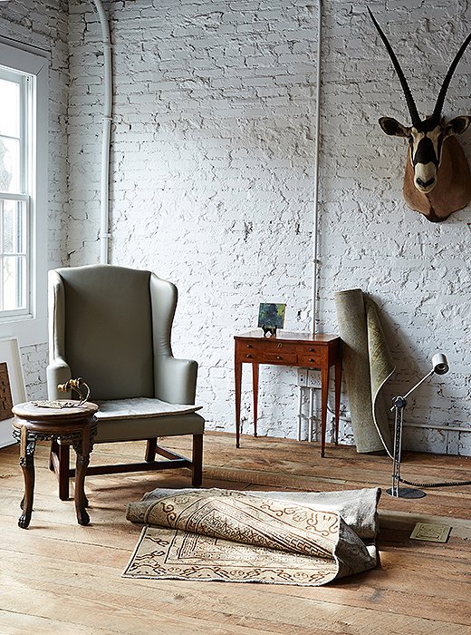 A table made of marble and carved wood pairs with a 19th-century wing chair reupholstered in leather and shirred velvet. Against the wall, the late 19th-century fruitwood sewing table is by French furniture maker Envio de E Kahn & Cie.
