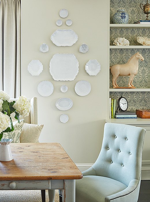 To carry the kitchen’s soothing color scheme into the adjacent areas, Jenny painted the base of her client’s antique farm table in a Farrow & Ball light blue (which matches a new coffered ceiling in the living room) and lined the dining room bookshelves with a soft blue-and-cream damask wallpaper.
