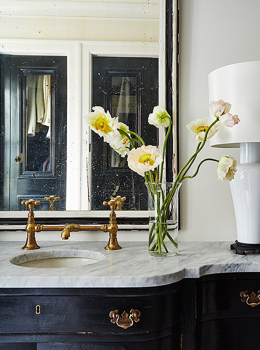 An antiqued mirror and gold fixtures are intermingled with white porcelain lamps on the sink vanity in the master bath, which is divided into a dressing room, a water closet, and a shower and tub room. “It was designed with a certain traffic mentality for getting ready quickly,” Darryl says of tailoring the space to fit his busy daily life. 
