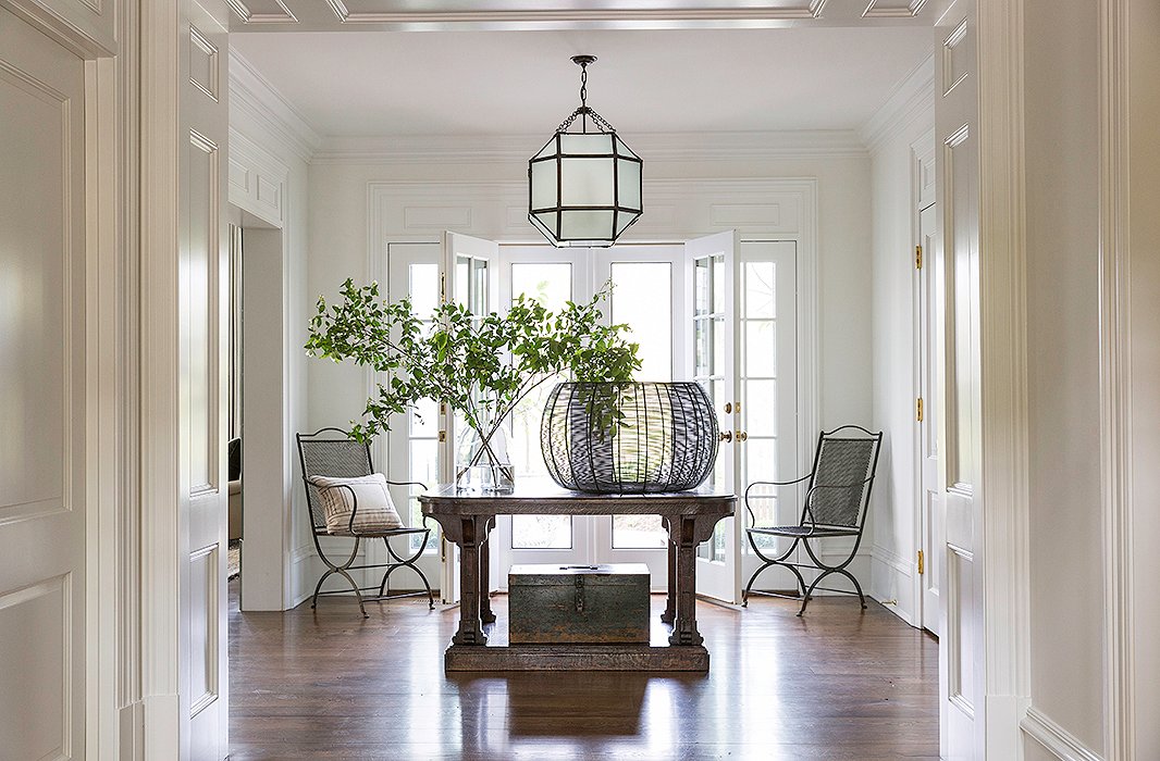With a center table, a pair of antique chairs, and a lantern by Suzanne Kasler, the house’s grand entrance hall is airy and inviting.
