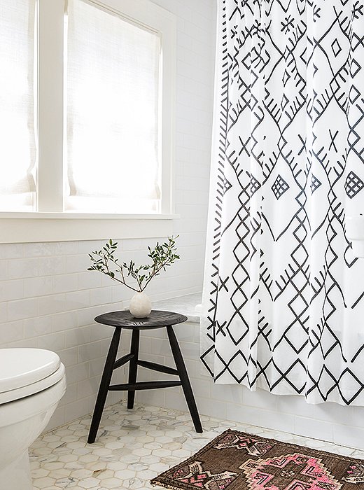 A small Persian rug and a petite black stool add a little contrast to the ultrawhite bathroom.
