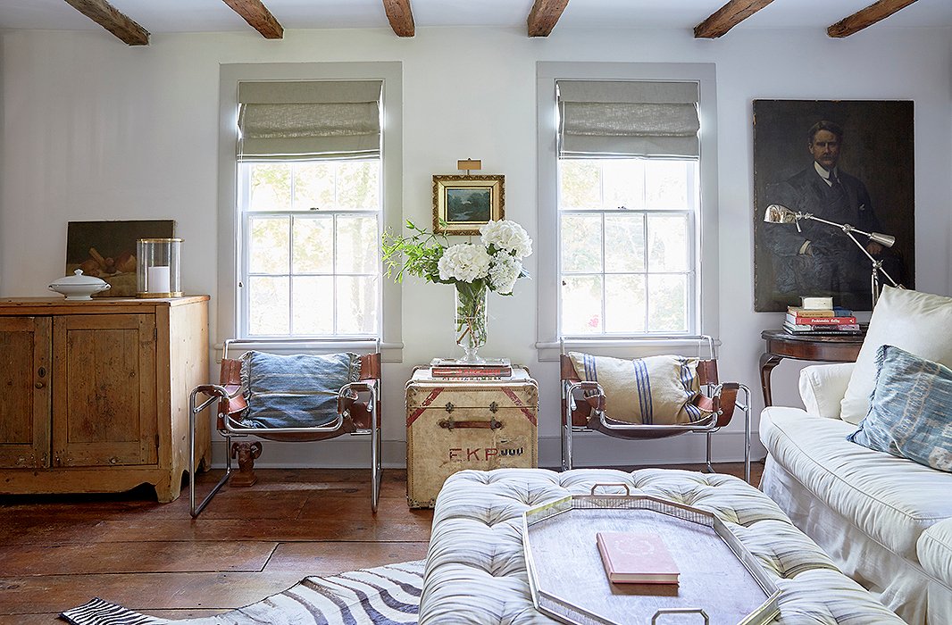 The living room is outfitted with a well-loved white sofa, a cozy tufted ottoman, and leather sling chairs for a little masculinity.
