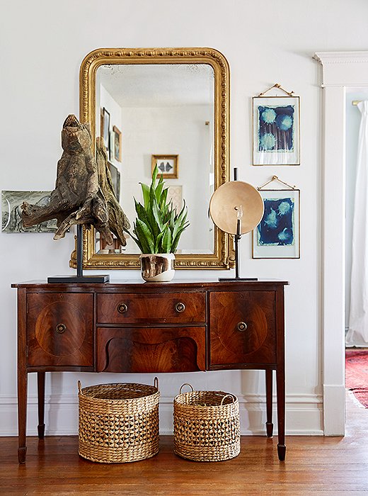 An antique burl-wood sideboard in the entry hallway is beautifully balanced by a Louis Philippe mirror, woven baskets, and original art.
