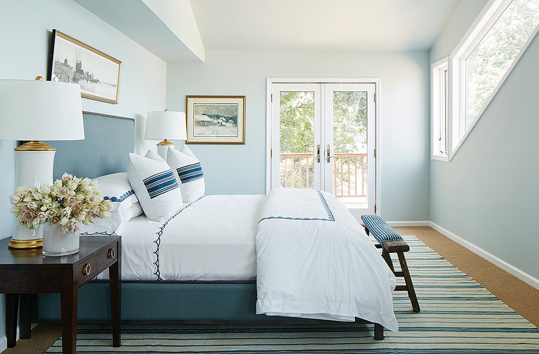 The narrow master bedroom was divided into sleeping and sitting areas. Crisp linens and vintage pillows dress the elegant bed. Find similar sheets here and the table lamps here.
