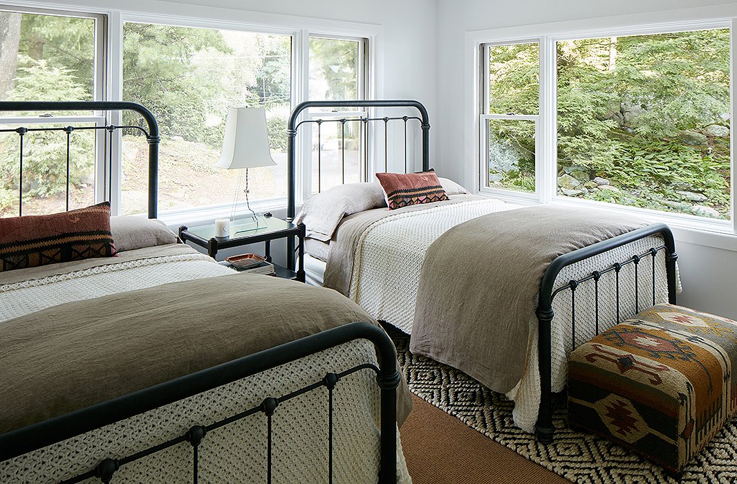 The twin guest rooms were designed to be durable and low maintenance. Cozy knit blankets and pillows made with vintage textiles warm up the iron beds. The designer used a “completely foolproof” jute rug on the floor.
 
