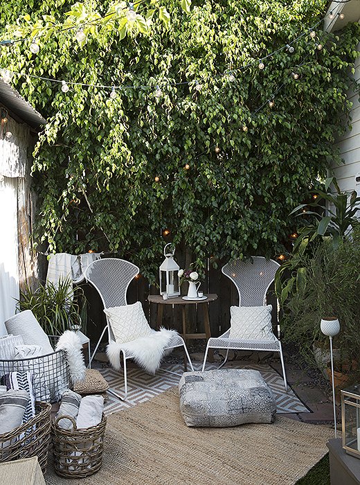 String lights are tucked among the garden’s foliage to create an otherworldly canopy. White votive candles and a lantern on the table add more glow factor after the sun sets.
