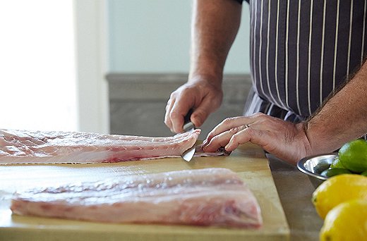 When putting the fish onto your cutting board, Greg says, “give it support; always use both hands.” Even firm-fleshed fish are delicate. Take a chef’s knife—not your sharpest one—and start at the tail end, slicing off just the skin on the bottom with a gentle back-and-forth motion.
