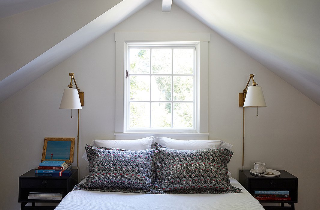 The most minimalist space in the home is the master bedroom. Because of the angular ceiling lines (“The architecture is the architecture”), Elizabeth chose not to dress the window, and the room couldn’t accommodate a headboard. “Besides, we’re up and out here and off to the beach, so I just kept it simple,” she says. She fell head over heels for the muted Liberty of London peacock-feather bedding, however. “It’s actually an odd choice for me, because I don’t do a lot of dark colors. But with the gray floor and white walls, it works.” The Graves Pivoting Sconces are similar to those above.
