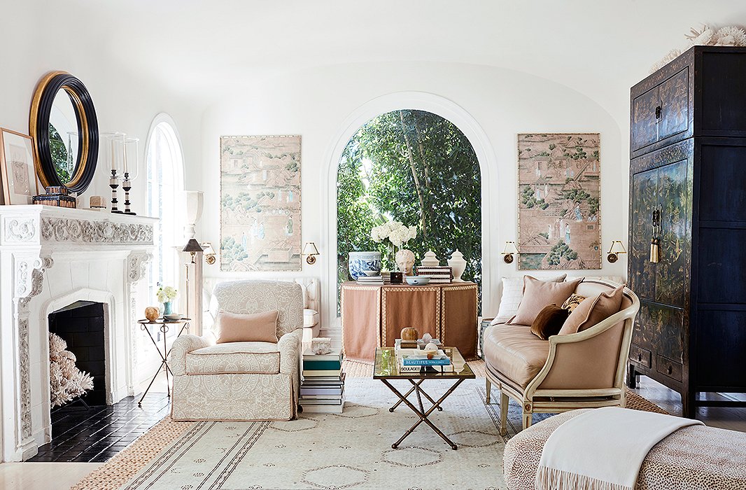 The wallpaper panels that flank the arched window inspired the overall design of the serene living room. “I love the pattern of these Gracie wallpaper panels. They really set the palette for the room,” Mark says. “The last time I redecorated I pulled the window treatments down because I really wanted the architecture of the room to open, and the arch windows are so beautiful.” An 18th-century chinoiserie armoire presides over the multiple seating areas.

