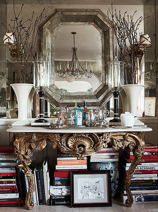 A gilded console at one end of the dining room houses a bar and more of Mark’s design books. “We don’t formally entertain,” he says. “So I wanted this to be a place where I could sit and work too.” The hurricane lamps are from his friend John Rosselli’s antiques shop. The custom mirror was made from antique glass.
