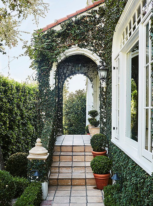 “I love to design homes that blend the indoors with the outside,” says Mark. “I think of outdoor spaces as additional rooms.” A tiled path lined with potted boxwoods leads to an enchanting entrance covered in creeping fig.
