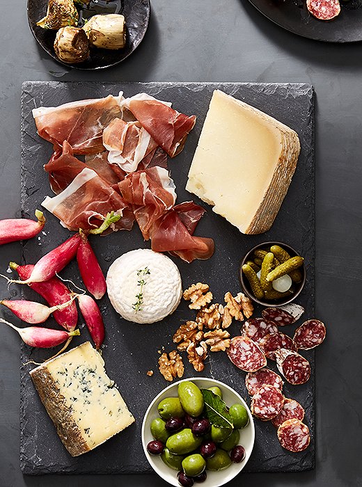 The dark slate board allows the beautiful colors of the radishes, olives, and meats to stand out.
