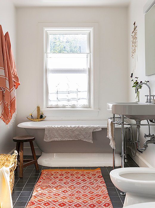 Orange fouta towels and a geometric rug add a splash of color to the kids’ bathroom.
