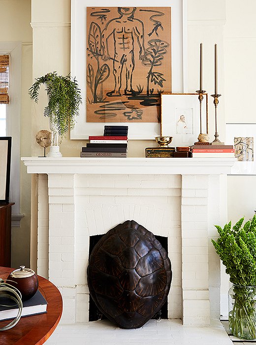 William used a tortoiseshell to hide the fireplace’s unsightly gas heater. The mantel is decorated with candlesticks he bought as a teenager and a brass vase that he updated with a coat of paint. “It’s the power of painting something white,” he says. “All of a sudden, it becomes really cool.”
