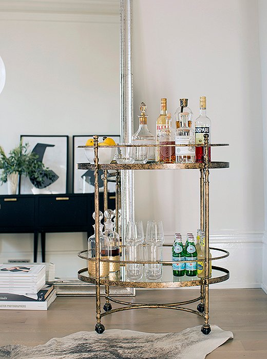 Leaned against the wall, an oversize silver mirror helps make the narrow room feel expansive—and plays off the metallic finish of the petite bar cart.
