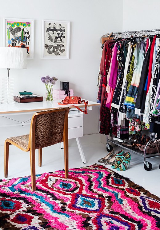 A cheetah-pattern chair and a colorful Moroccan rag rug are tempered by the simplicity of a white table and a Lucite lamp. Closet space is limited, so a rack holds the overflow in this corner space.
