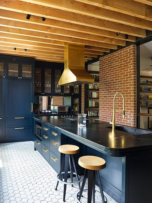 The dark kitchen, painted Farrow & Ball Black Blue, doesn’t feel so dark with a wall of windows and a mirrored backsplash to reflect light around the space. The untreated wood beams introduce a more natural vibe.
