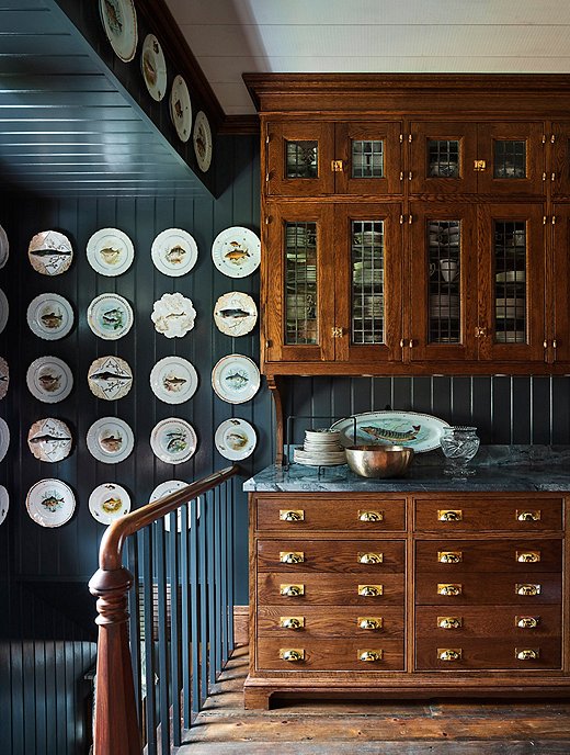 One of Philip’s favorite spaces in the house is the servery, attached to the dining room. Painted dark gray-blue and adorned with a collection of Limoges fish plates, the servery enables Philip and Mark to store the substantial collection of dishware they amassed and inherited over the years. “It’s the first house we’ve been in that has a space for all our serveware,” Philip says.
