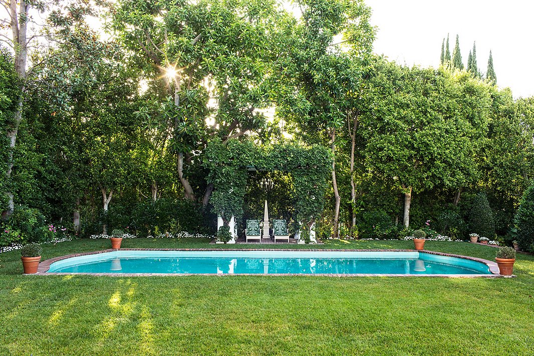 A wisteria-covered pergola, accented with a chandelier and upholstered chairs, creates an elegant outdoor living room. Photo by Nicole LaMotte.
