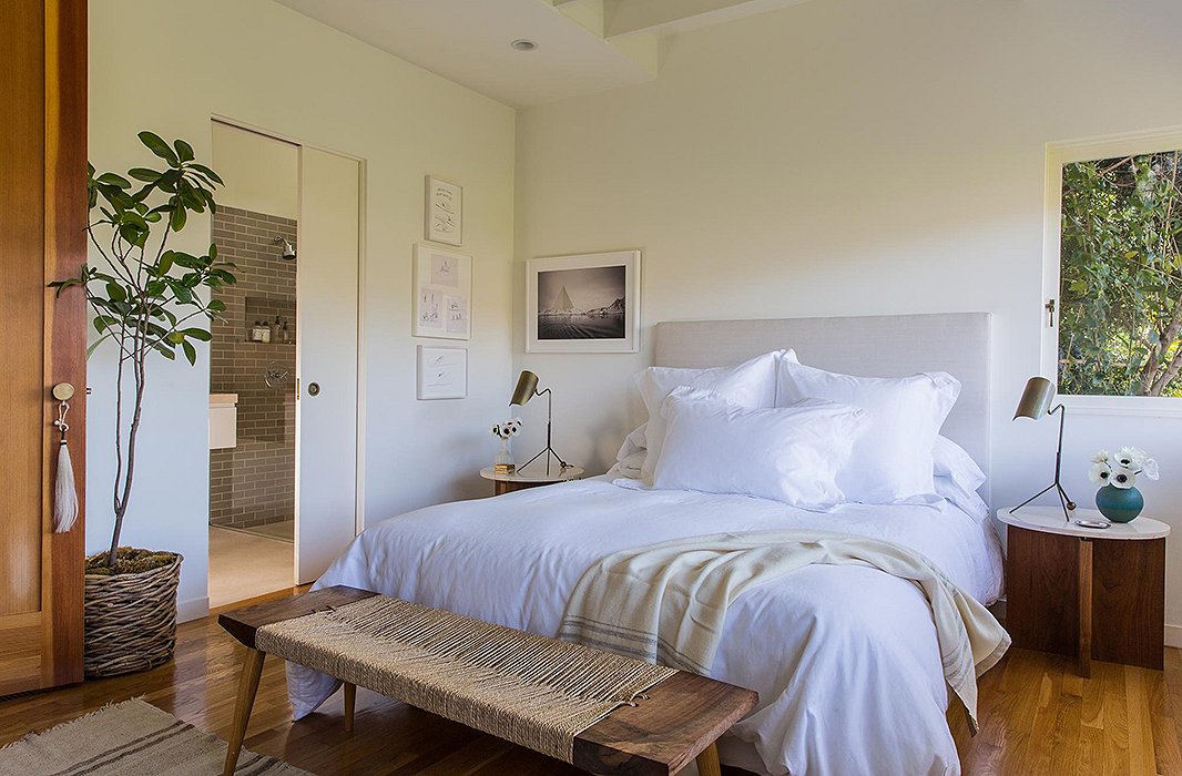 Jessica wanted “a little more ceiling height and lots of natural light” for the master bedroom, making it “a refuge to relax in.” A linen-covered headboard and white bedding keep it airy. A custom bench by Mark Coppos and artwork by Russell Crotty and Sarah Anne Johnson add delicate pattern and texture.
