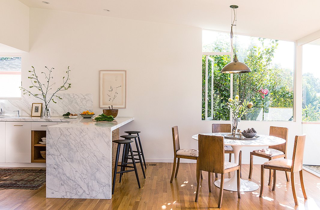 The open dining area suits the couple’s entertaining style. “We like to serve family style so that people can make themselves at home,” says Jessica. Stools from Sawkill Co. under a Carrara marble bar and a Michael Snow print make for a nice breakfast spot. 