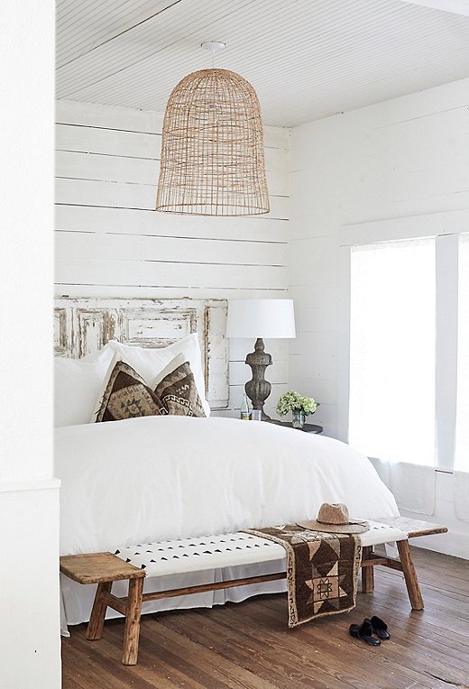 A bench upholstered in mud cloth from Mali rests at the foot of the bed in the Found Cottage suite, which features a distressed-wood door as its headboard. 
