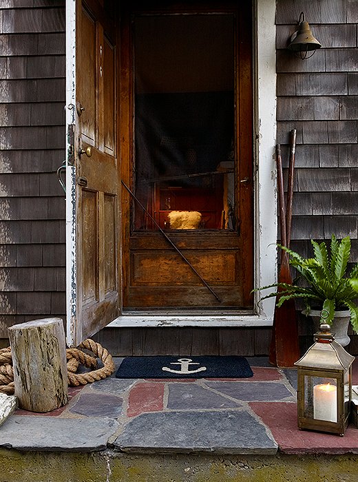 Outside, a gravel path leads to a slate porch. Styled with an old tree stump, an anchor mat, and a brass lantern, it hints at the nautical charm found within. 
